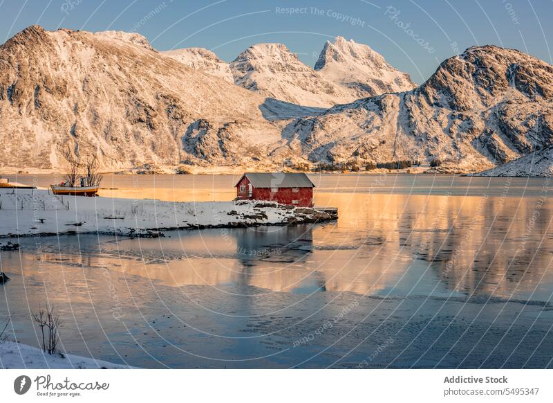 House on shore near water against mountains in winter landscape ridge sea formation house cottage rocky snow cold freeze scenery seashore lofoten island norway