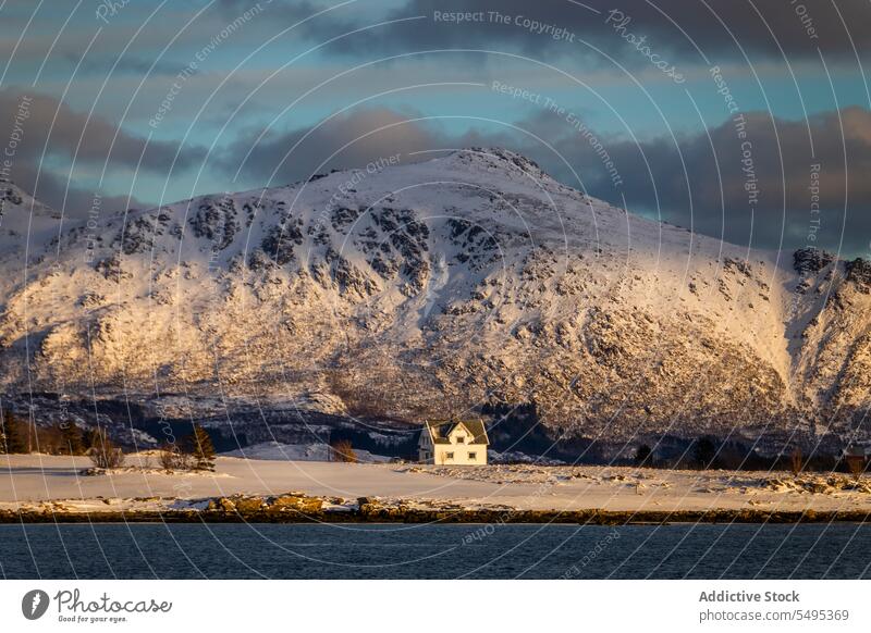 Lonely house near snowy mountain slope winter ridge nature picturesque landscape lake weather norway lofoten island north residential scenery building cloudy