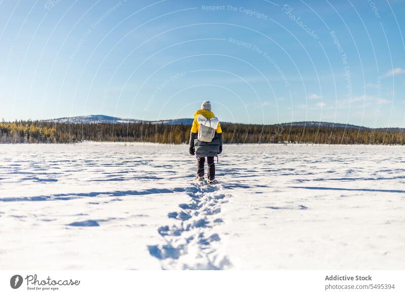 Anonymous traveler walking on snowy ground in winter tourist hiker nature explore footprint warm clothes field norway blue sky tourism backpack landscape