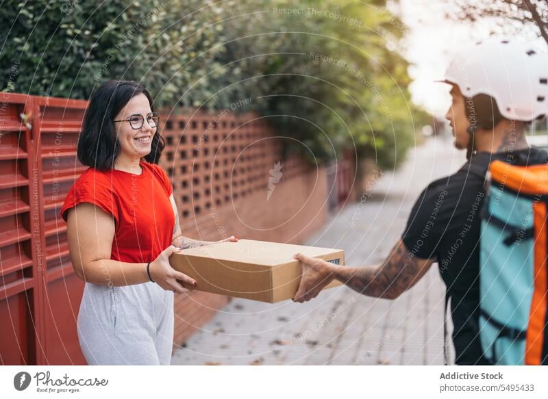 Happy customer receiving parcel from courier on sidewalk woman delivery man receive cardboard box smile package service protect safety shipping cheerful casual