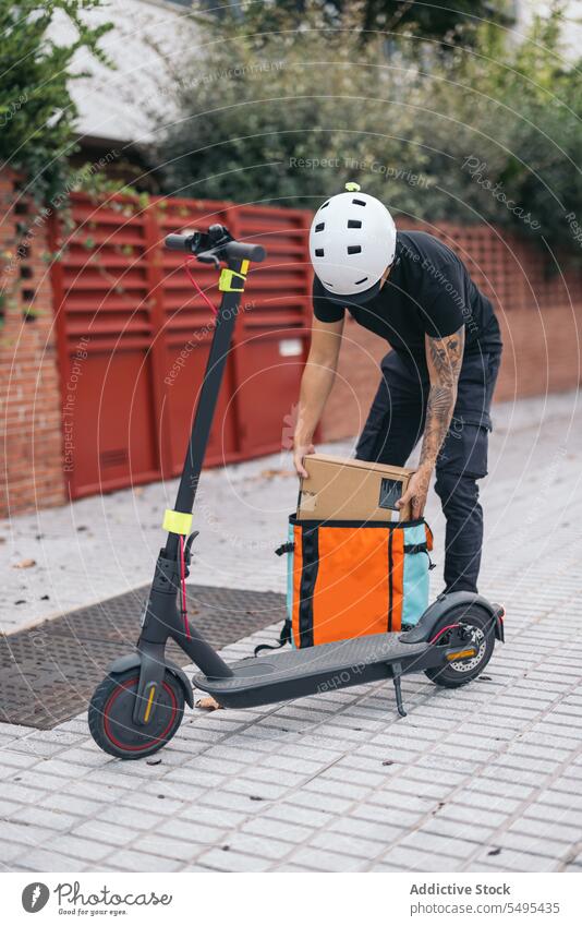 Male courier with box near electric kick scooter delivery man remove bag transport eco friendly pavement modern vehicle package town service helmet shipment