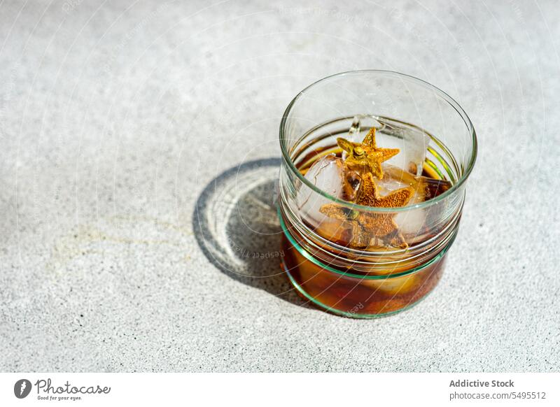 Glass of whiskey with ice and orange peel on gray surface glass shape star container transparent high angle from above blur blurred background fruit drink cool
