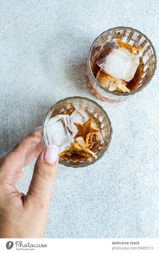Anonymous person with glasses of whiskey with ice and orange peel shape star container transparent crop high angle from above blur blurred background fruit