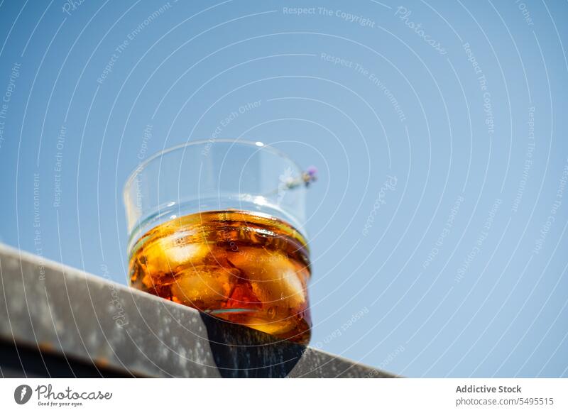 Glass of whiskey with ice and orange peel against blue sky glass container transparent blur blurred background fruit drink cool cold beverage alcohol alcoholic