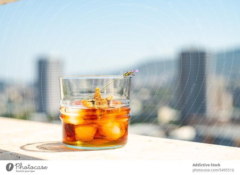 Glass of whiskey with ice and orange peel on white surface against blurred city glass shape star container transparent blurred background fruit drink cool cold