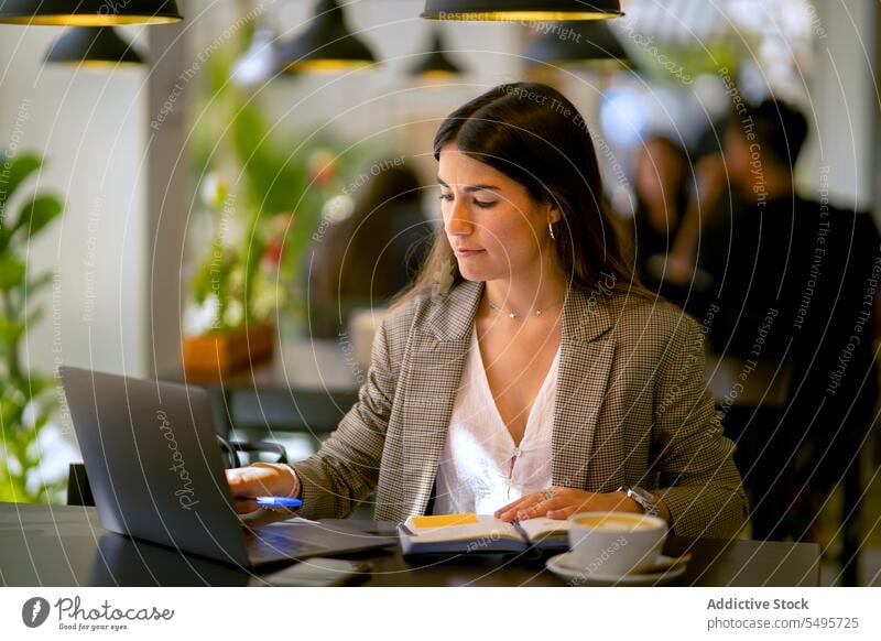 Focused woman working on laptop with coffee in cafe freelance remote project concentrate planner notebook job young female device using gadget netbook computer