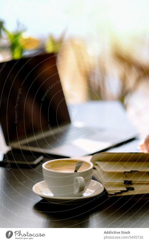 Cup of coffee on table and book with laptop on table cappuccino cup hot drink spoon notebook cafe smartphone workspace morning modern cafeteria planner