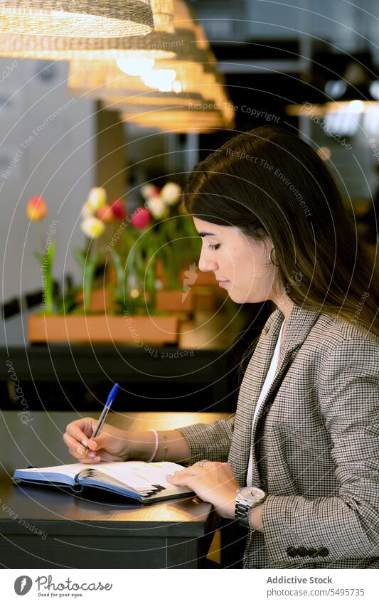 Focused young woman sitting at table and making notes in cafe take note write notebook smile notepad planner pen female positive free time cafeteria optimist