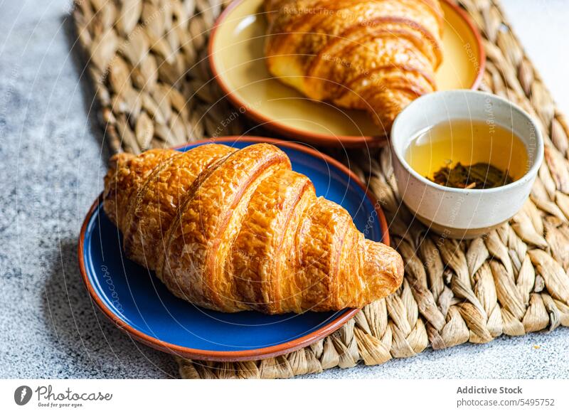 Fresh baked croissants on ceramic plates fresh colorful brown napkin cup green tea table surface gray background high angle from above food drink beverage hot