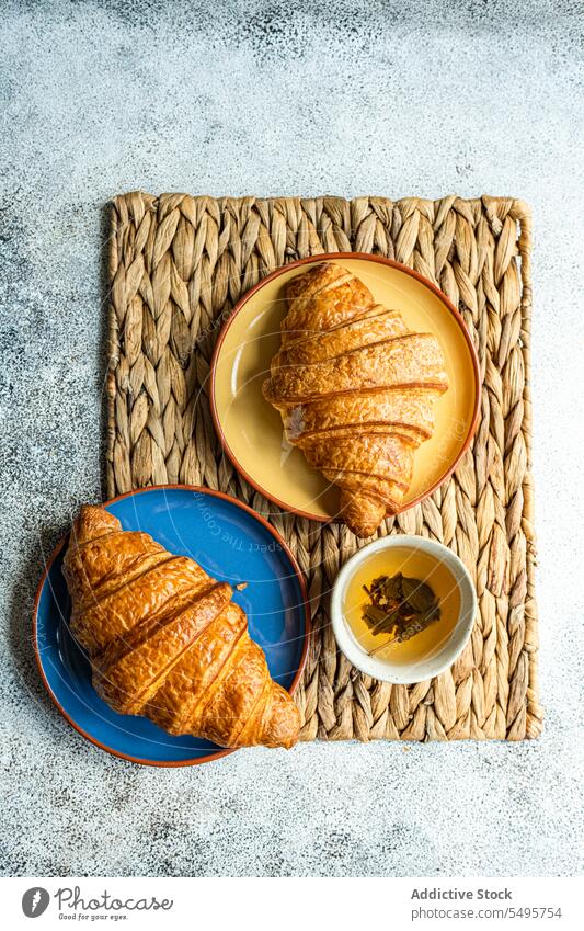 Fresh baked croissants on ceramic plates fresh colorful brown napkin cup green tea table surface gray background high angle from above top view food drink