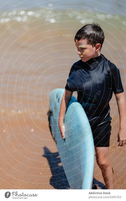 Boy with surfboard in sea kid surfer activity ocean water shallow hobby summer nature enjoy vacation sporty beach holiday child lifestyle face paint active male