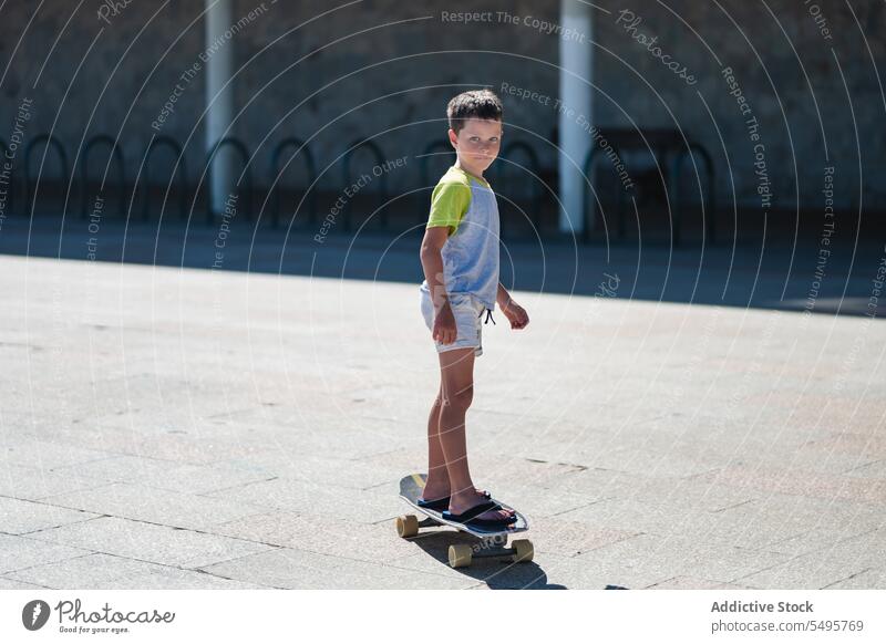 Boy riding longboard on street boy ride activity hobby skater kid casual happy child cute childhood lifestyle trendy summer carefree energy pavement balance
