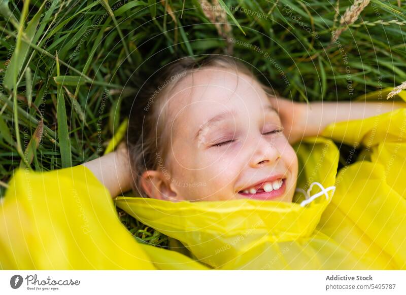 Little cute girl lying on green grass kid laugh nature happy meadow enjoy child having fun play little raincoat childhood positive content activity playful