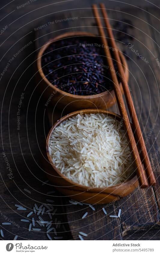 Raw wild black rice and peeled white rice in the bowls with chopsticks. raw table surface food served menu meal lunch dinner ingredient dish cuisine healthy