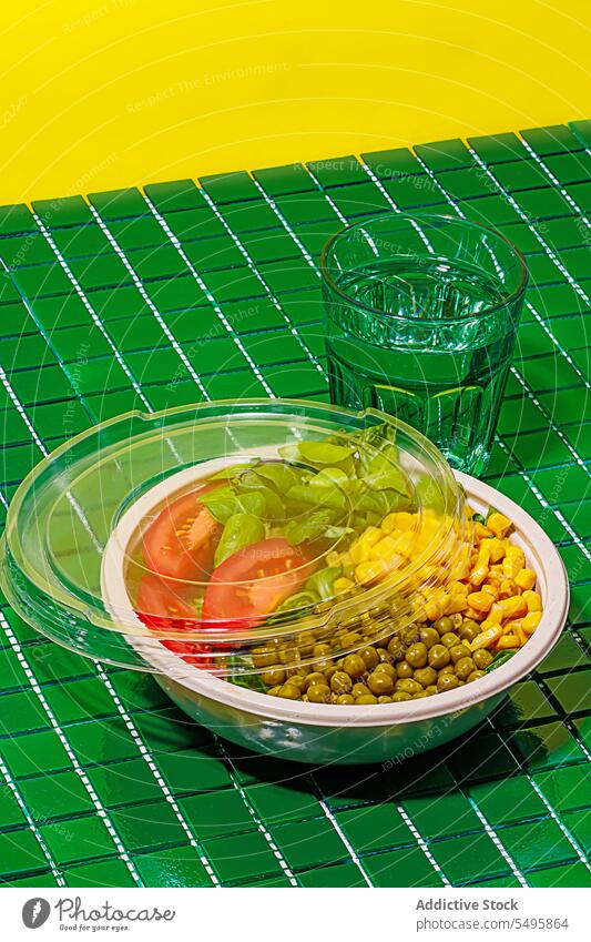 Salad bowl on green background with plastic cover near glass of water salad food slice tomato spinach leaf corn kernel pea colorful surface table healthy eat