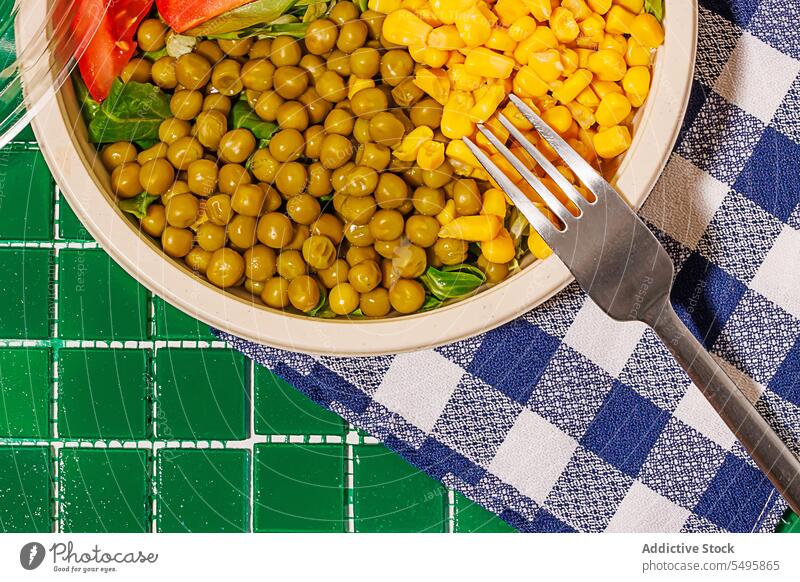 Salad bowl on napkin on green background with plastic cover and fork salad food slice tomato spinach leaf corn kernel pea colorful surface table healthy eat