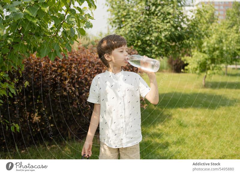 Thirsty boy drinking water from bottle in park thirsty summer child eyes closed plant weekend lifestyle cute children nature plastic green refreshment childhood