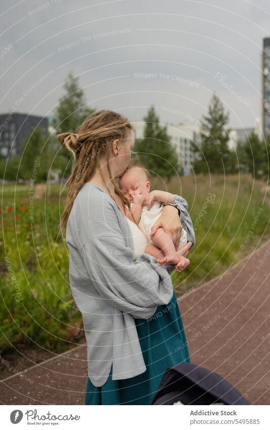 Woman carrying and kissing baby in park against sky mother head woman love small hug adorable family lifestyle cute dreadlocks infant together cuddle motherhood