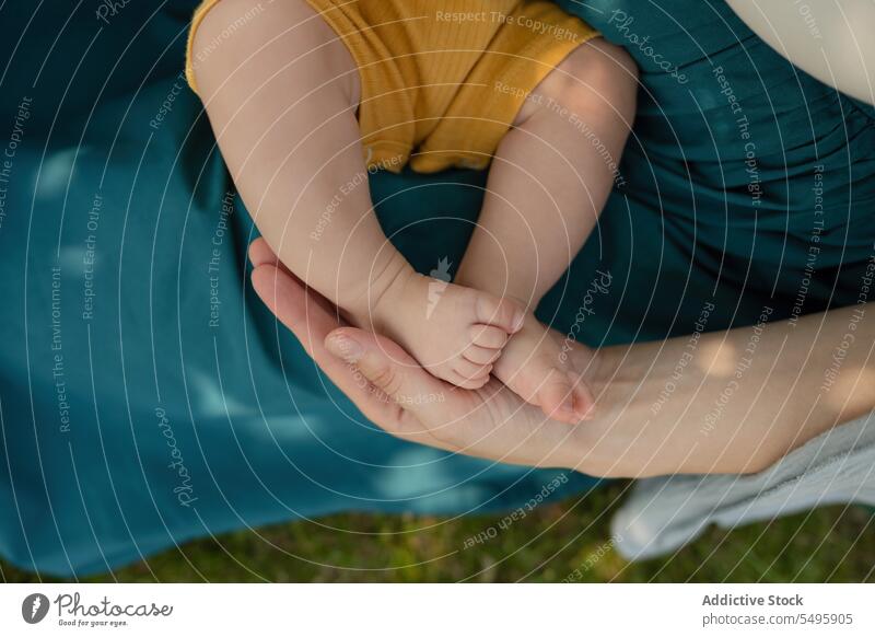 Hand of mother holding baby's legs while sitting in park woman hand crop family tender love body part together infant weekend motherhood care affection eltern