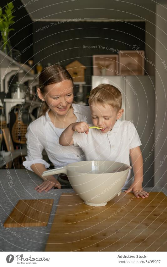 Happy mother looking at son tasting food in kitchen smile cooking woman boy family spoon mixing bowl countertop love free time home happy sweet dessert prepare