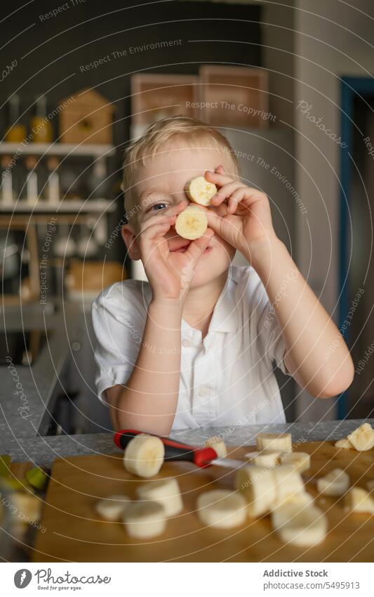 Boy holding banana slices in front of face in kitchen boy cook child prepare cute playful piece cutting fruit chopping board food lifestyle innocence childhood