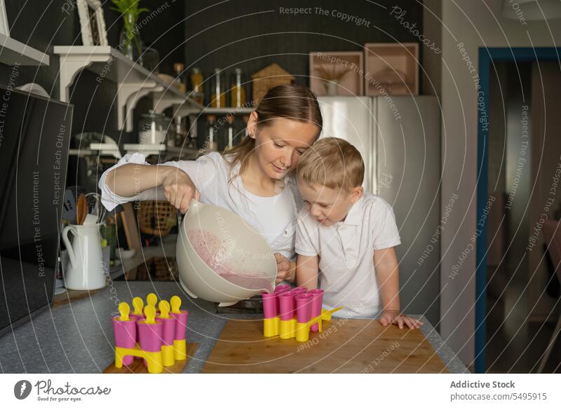 Boy looking at woman making ice cream in kitchen mother son pouring liquid boy popsicle molded blonde hair family curious sweet food free time female dessert