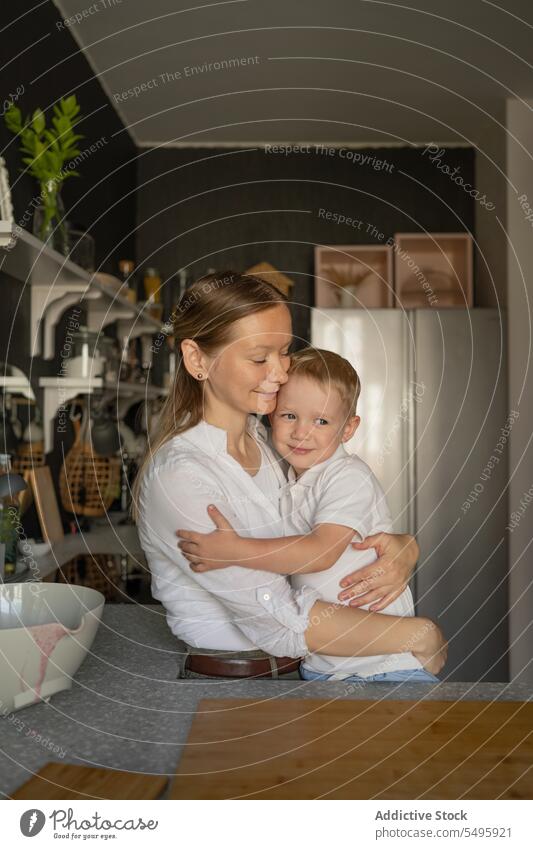 Mum hugging her son in the kitchen mother cute woman boy weekend smile love family child bowl food lifestyle affection happy casual attire bonding innocence