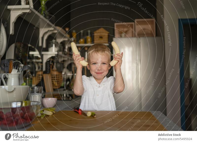 Cute boy holding bananas and smiling in kitchen cooking cute portrait child fruit preparation lifestyle food innocence childhood home blonde hair knife peel