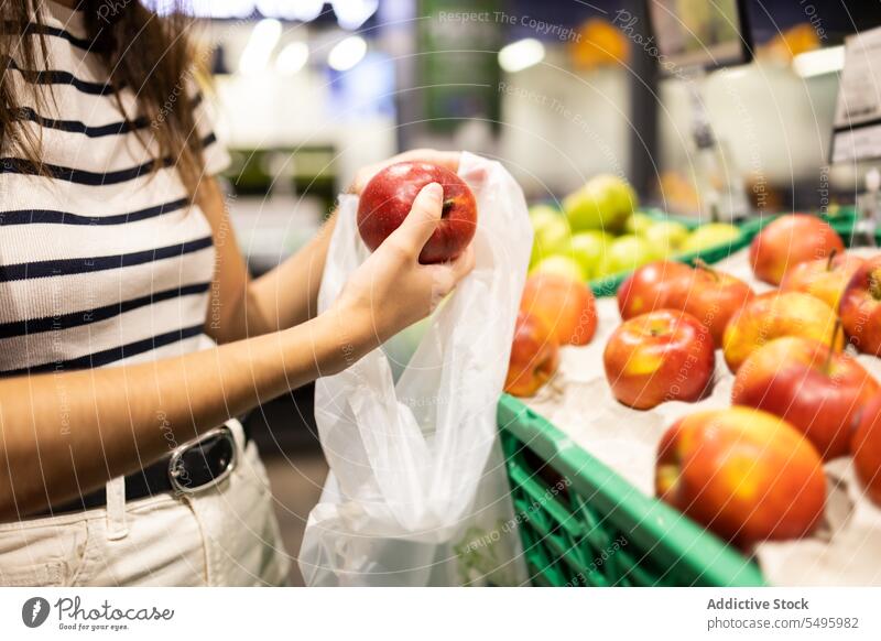 Crop woman choosing apples in grocery store choose buy put market fruit bag purchase customer fresh organic ripe buyer local food casual red tasty choice female