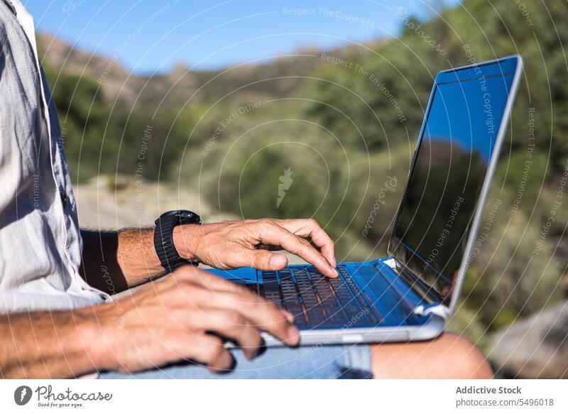 Anonymous crop man using laptop on rocky cliff freelance work nature browsing traveler male plant remote gadget summer device internet surfing computer online