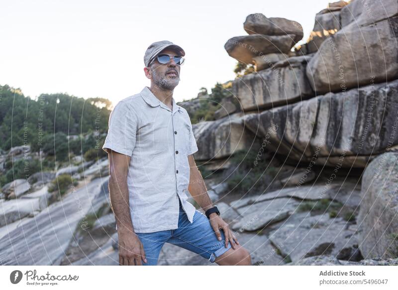 Serious man in sunglasses standing on rocky terrain nature serious evening summer environment travel natural male cap beard sunset unshaven accessory explore