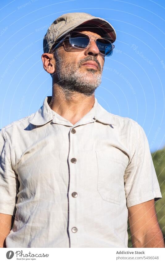 Confident bearded man in sunglasses and cap confident summer blue sky serious brutal appearance male unshaven individuality nature eyewear personality accessory