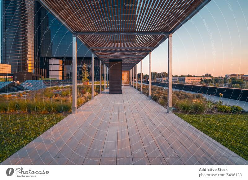 Empty walkway between modern buildings with columns in daylight grass river park sunset bush exterior water structure construction architecture blue sky facade