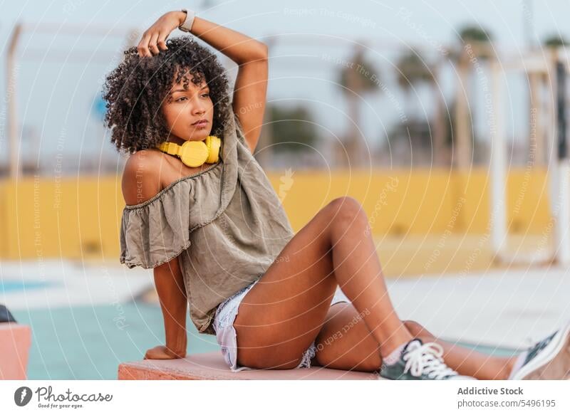 Curly haired female touching hair while relaxing on bench woman thoughtful pensive serious think confident sit dreamy curly hair lifestyle elegant apparel
