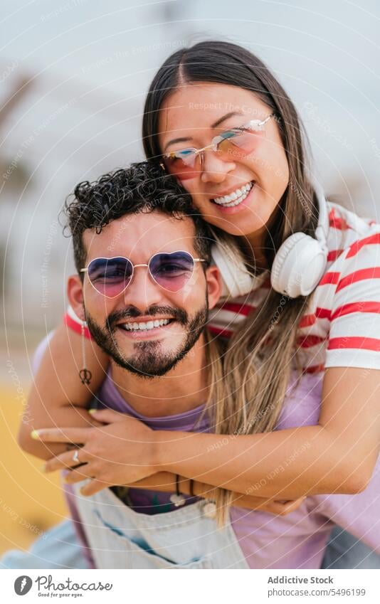 Friends piggybacking and smiling couple hug street happy smile love relationship sunglasses romantic date together embrace headset boyfriend friendly positive