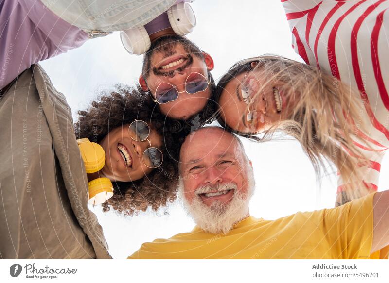 Low angle of excited diverse family hugging and looking at camera friend laugh having fun people friendship group unity sunglasses eyewear headset happy embrace