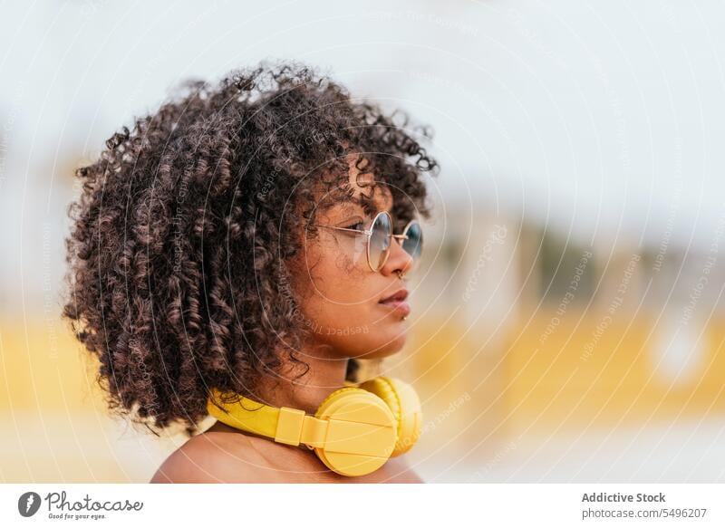 Young woman with headphones and eyeglasses curly hairstyle looking forward eyewear headshot pensive portrait headset audio trendy alone human face concentrate