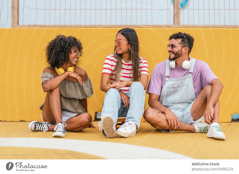 Diverse friends in headphones sitting on floor positive street style music smile ground yellow diverse friendship trendy eyewear cool lifestyle modern group