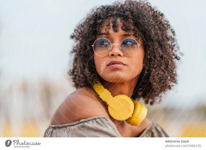 Young woman with headphones and eyeglasses curly hairstyle looking away eyewear headshot pensive portrait headset audio trendy alone human face concentrate