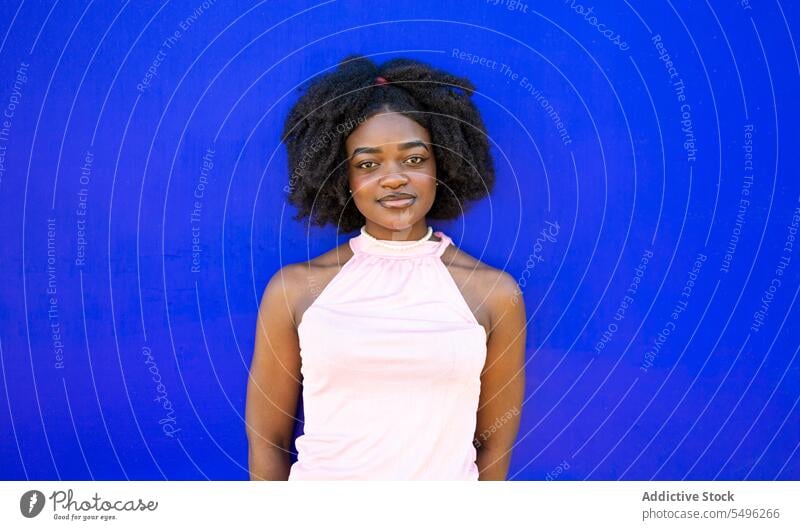 Smiling black teenage girl in casual dress on blue background portrait afro hairstyle appearance makeup curly hair calm young female ethnic model hairdo