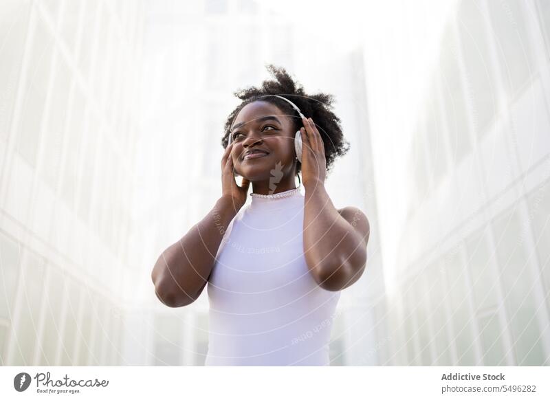 Cheerful black teenage girl touching headphones listen music street song enjoy afro positive gadget device smile playlist female ethnic african american happy