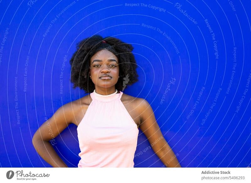 Smiling black teenage girl in casual dress on blue background portrait afro hairstyle appearance makeup curly hair calm young female ethnic model hairdo