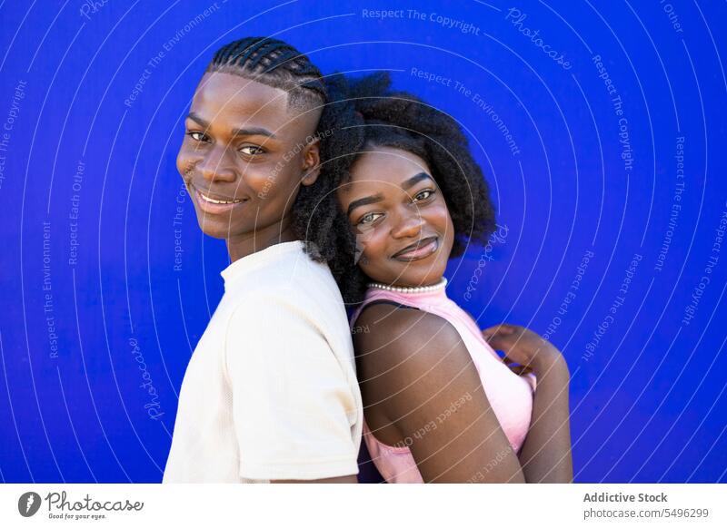 Cheerful black teenage couple leaning back to back afro together positive relationship hairstyle appearance smile portrait casual girlfriend boyfriend