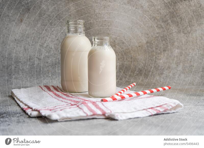 Raw cow milk in vintage bottles on rustic napkin and drinking straws gray surface white glass transparent fresh product beverage breakfast nutrition container