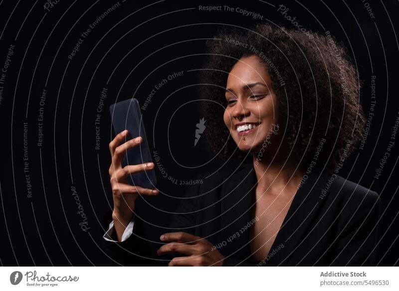 Smiling ethnic woman with smartphone in black studio using browsing smile happy positive online message mobile hispanic female young gadget device cheerful
