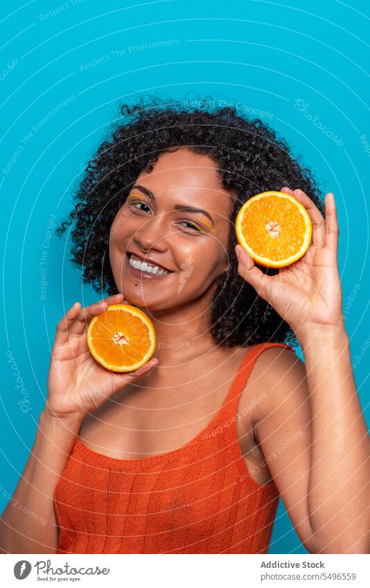 Cheerful ethnic woman with orange slices in blue studio smile fruit skin care beauty happy portrait positive curly hair young summer female hispanic cheerful