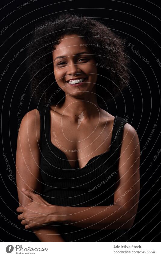 Smiling ethnic woman looking at camera in dark studio positive smile appearance leisure carefree happy afro curly hair friendly young female charming glad
