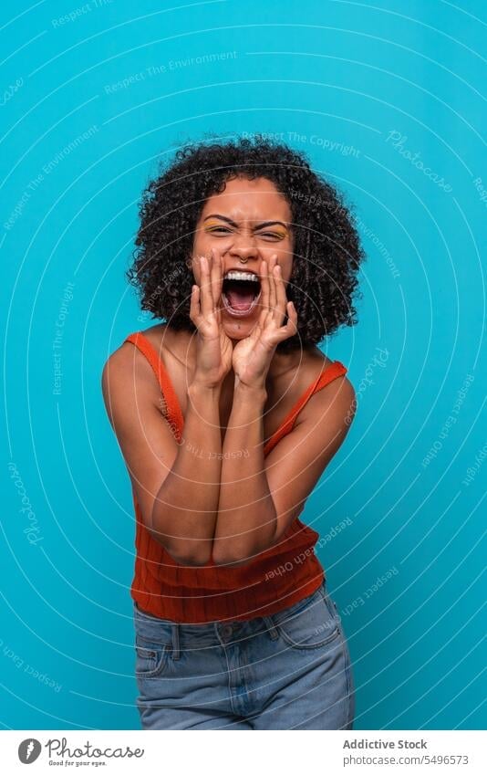 Excited black woman screaming at blue wall model afro shout support joy excited portrait female african american yell dark hair brunette curly hair hairstyle