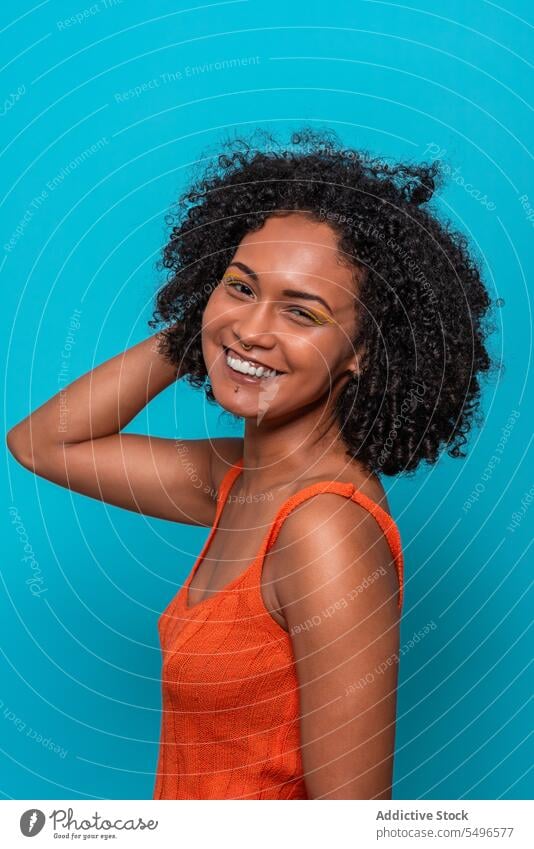 Smiling black woman in orange top looking at camera fashion model slim slender dark hair curly hair female african american outfit cloth wear casual brunette