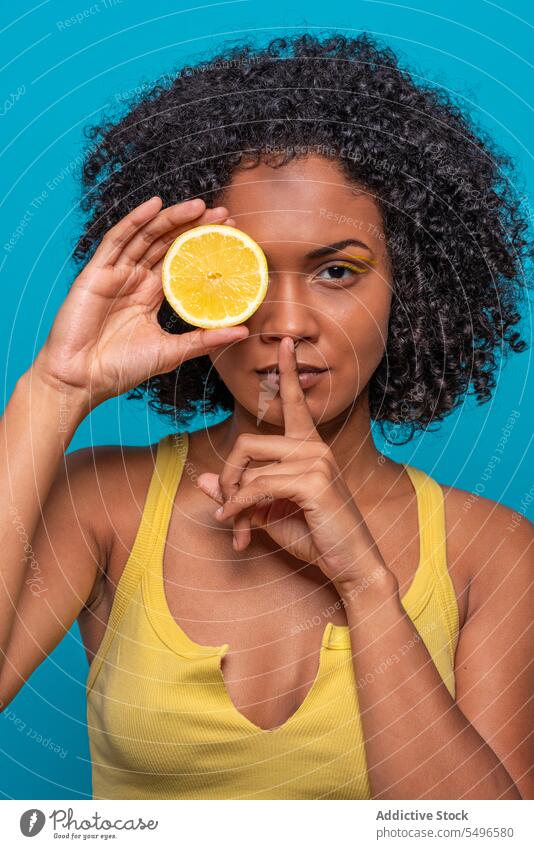 Woman covering eye with orange slice and gesturing silence woman cover eye portrait gesture silent fruit secret skin care citrus bright young curly hair female